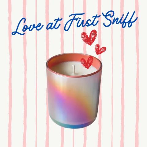 An iridescent candle jar with red heart illustrations and the text "Love at First Sniff" against a pink and white striped background.