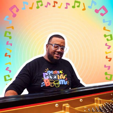 Photo of Mister Boom Boom playing a keyboard against an arch of music notes.